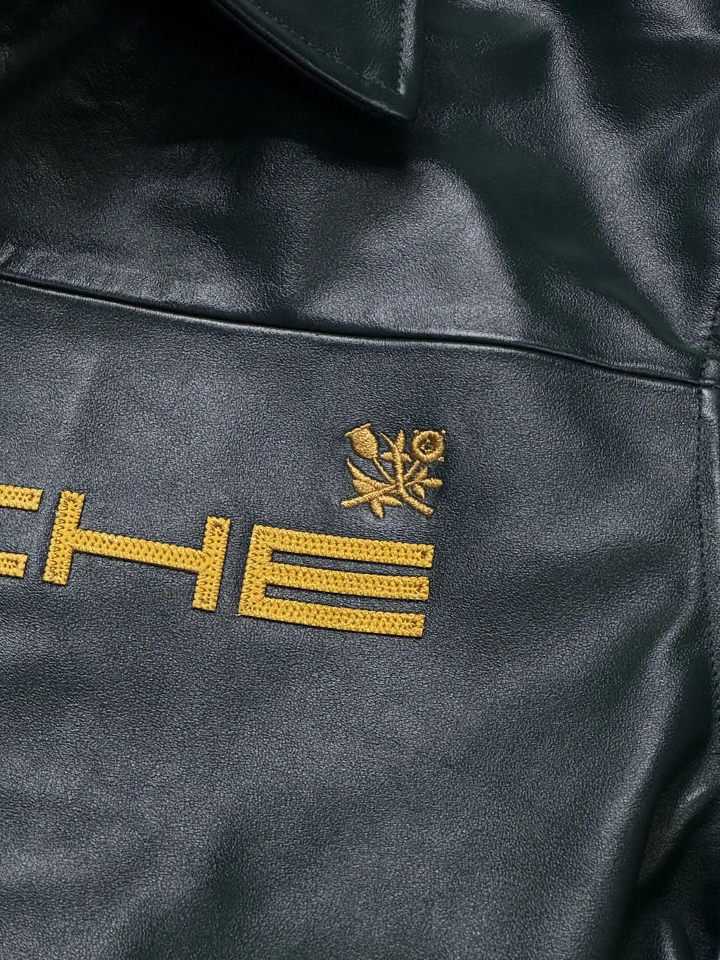 Close-up of a stitching detail on Porsche leather jacket with gold embroidery on a dark background