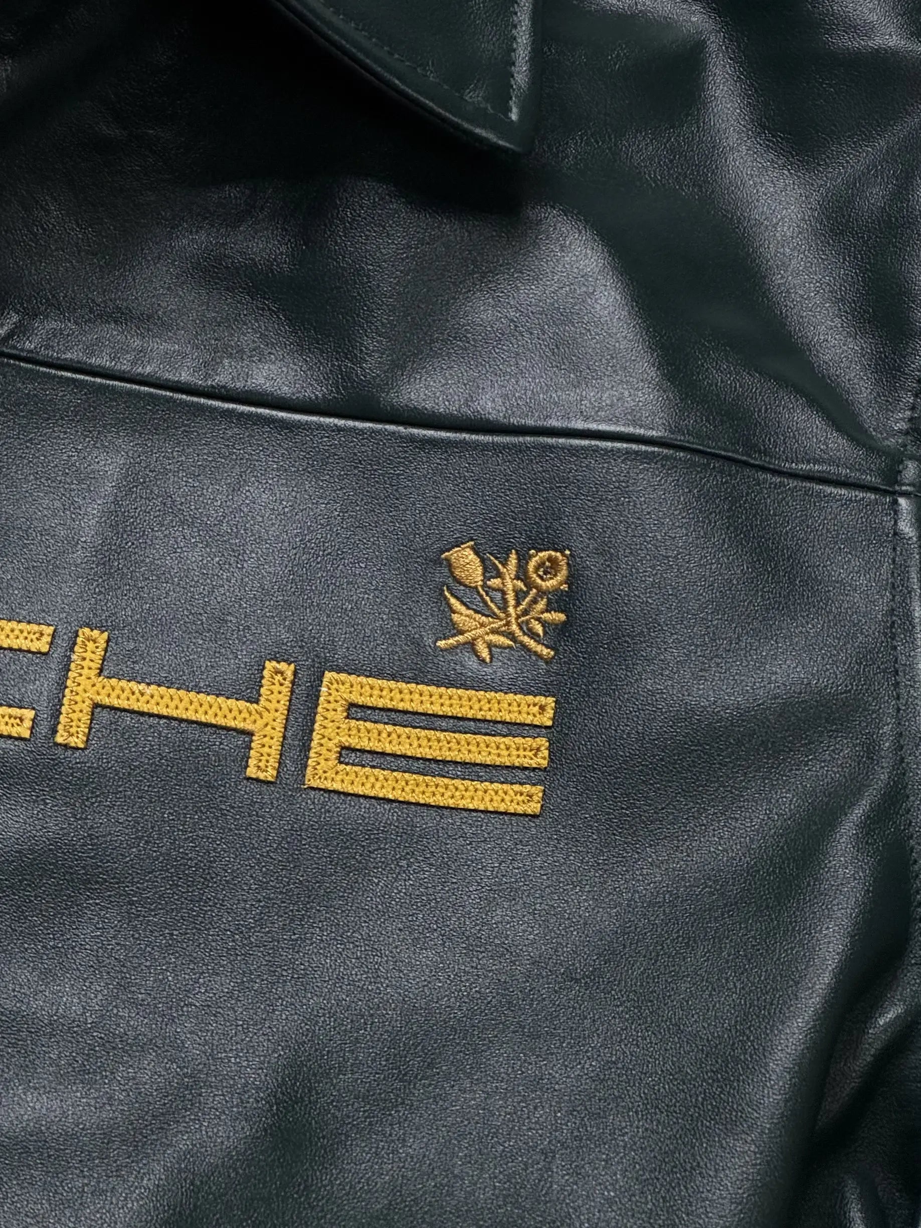 Close-up of a stitching detail on Porsche leather jacket with gold embroidery on a dark background