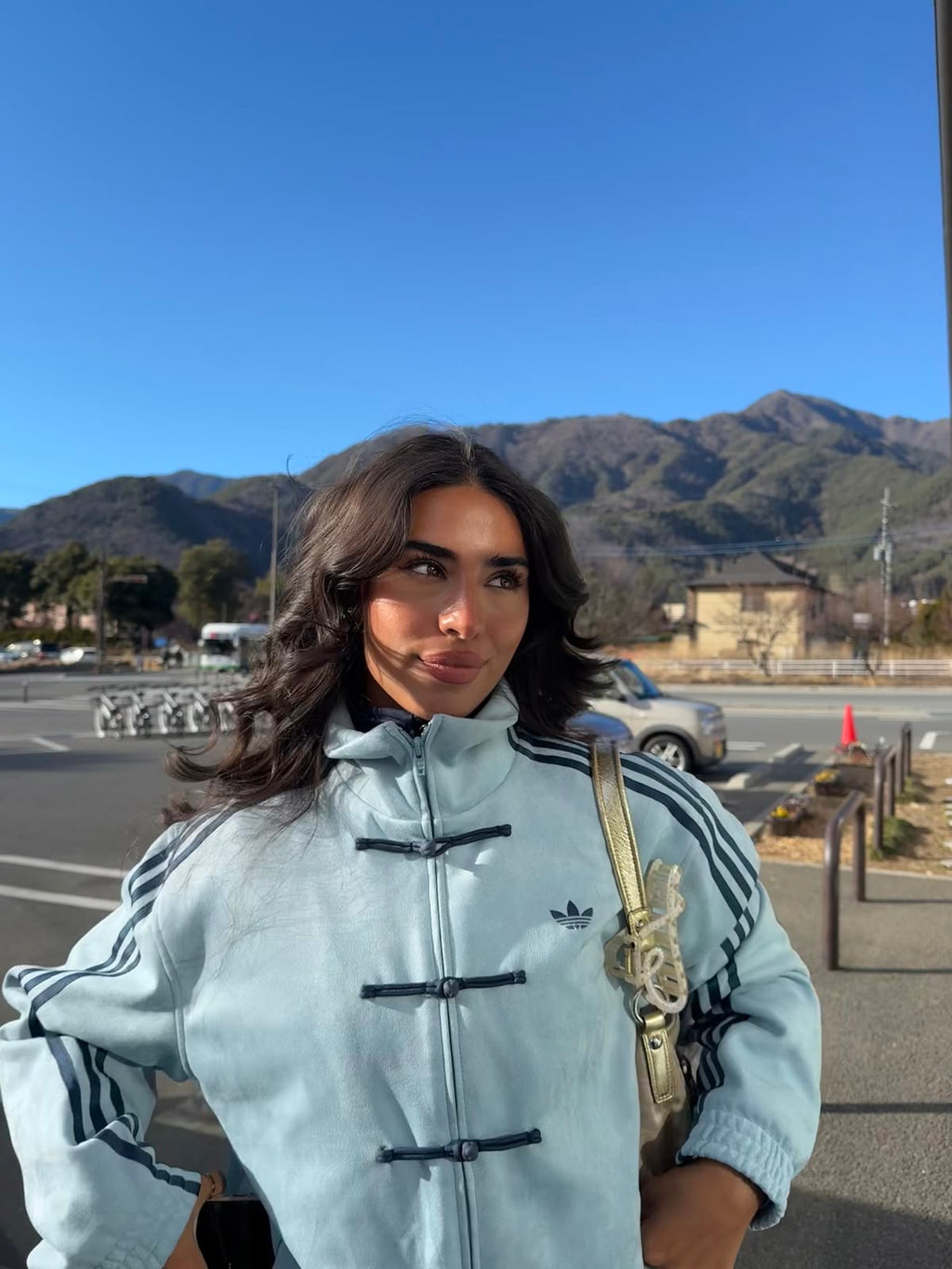 Woman wearing the sky blue CNY jacket outdoors in winter light, collar zipped with knot buttons fastened