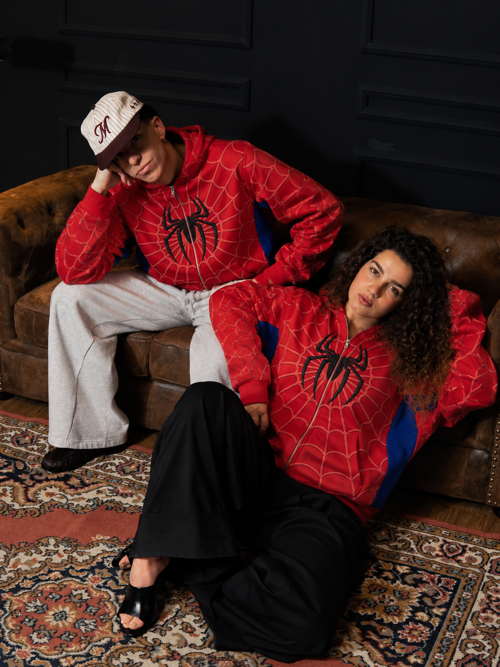 Matching spider print hoodie outfits on a leather couch, styled with grey sweatpants and wide black trousers